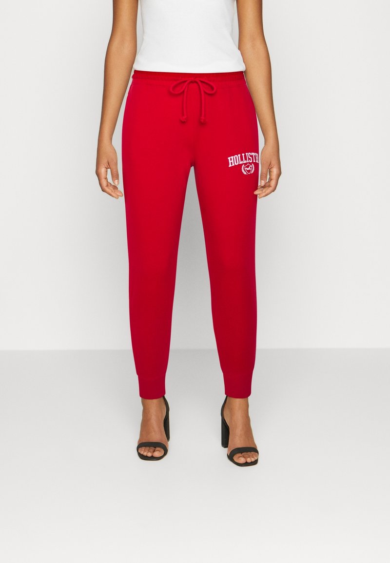 Röda joggarbyxor i mjukt tyg, med dragsko i midjan och en vit "Hollister"-logotyp på fram vänster. Åtsittande muddar vid anklarna.