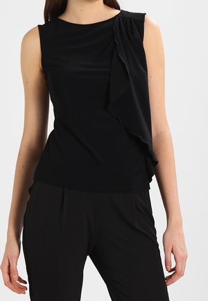 Top noir sans manches en tissu lisse, avec un détail volanté sur le côté et une coupe ajustée. Associé à un pantalon noir tailleur.