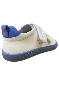 Zapatilla blanca de cuero con talón azul, banda de velcro, detalles perforados y suela de goma gris. Logo de la marca en el lateral.