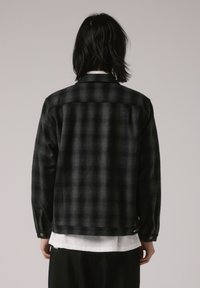 Chemise en flanelle à carreaux noir et gris, avec des poignets à boutons, coupe droite, tissu de poids moyen et texture lisse, présentant un motif à carreaux subtil.