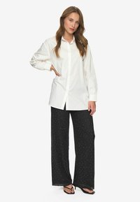 White button-up shirt with long sleeves, paired with loose black pants featuring white polka dots. Simple design, cotton material.