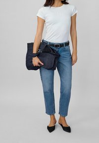 Vit t-shirt med kort ärm och en subtil logotyp, tillsammans med blå denimjeans och en väska i mörk denim. Svarta spetsskor avslutar looken.