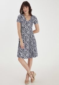 Navy i białe sukienka w paski zebry z krótkim rękawem, dekoltem w kształcie litery V i rozkloszowanym dołem, w połączeniu z beżowymi sandałami na koturnie. Miękki, elastyczny materiał.