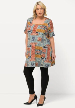 Monivärinen tunika, jossa on geometrisia kuvioita punaisessa, sinisessä ja keltaisessa; tippukollimi ja lyhyet hihat, yhdistettynä mustiin legginsseihin.