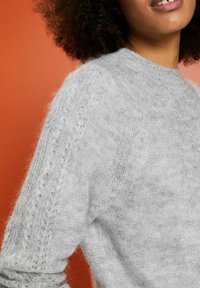Lichtgrijze gebreide trui met een textuurpatroon en geribbelde details. Zachte, fuzzy stof met een ronde hals.