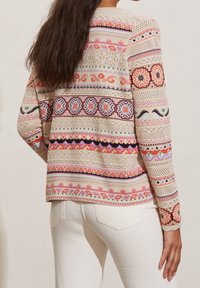 Pull en maille avec motifs horizontaux multicolores, comprenant des dessins floraux et géométriques, avec une base beige clair et des manches longues.