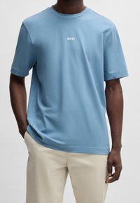 Světlomodré krátké tričko s krátkým rukávem z bavlny, s kulatým výstřihem a bílým logem "BOSS" na hrudi. Hladká textura.