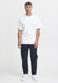 Vit t-shirt med kort ärm och rund halsringning, i kombination med mörkblå byxor och vita sneakers. Enkelt mönster och avslappnad passform.