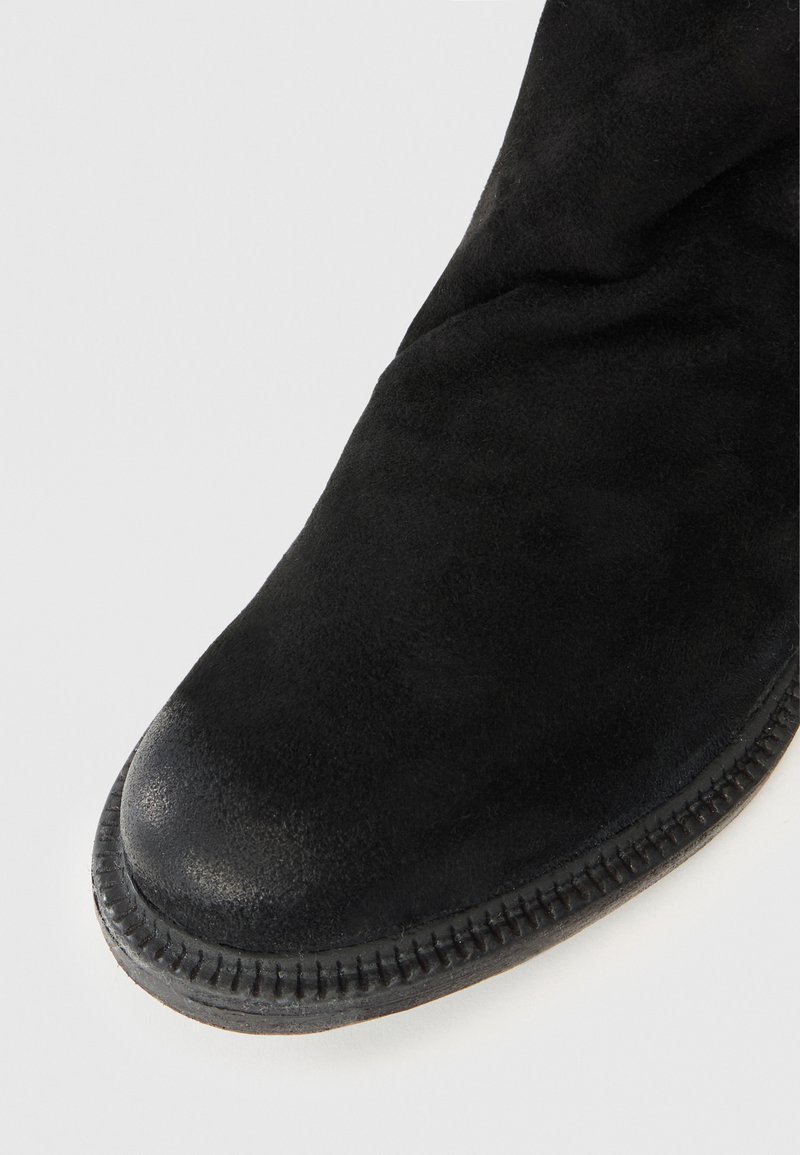 Primo piano della parte anteriore di un boot in suede nero con cuciture dettagliate sul bordo della soletta.