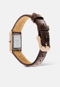 Reloj rectangular de oro rosa con correa de cuero texturizado marrón oscuro y hebilla dorada, mostrado desde la parte trasera con la marca y el número de serie visibles.