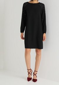 Svart långärmad klänning med rund halsringning och smyckade detaljer på axlarna. Kombinerad med bordeauxfärgade strappy högklackade skor.