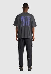 Czarnoszary, oversizowy t-shirt z niebieskim nadrukiem na plecach. W zestawie z czarnymi spodniami cargo i ciemnym obuwiem.