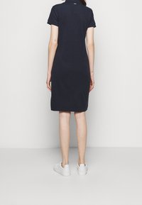 Námořnické polo šaty s krátkými rukávy a límcovým výstřihem, s rovnou siluetou a bočními rozparky, doplněné bílými teniskami.