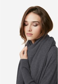 Grå, strikket sweater med høj krave, ribbede ærmer og en løs pasform. Stoffet virker blødt og struktureret, velegnet til lagdeling.