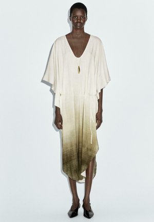 Robe en lin beige avec un col en V profond, manches courtes larges, et un effet ombré vert olive progressif. Elle possède une taille à cordon et un ourlet asymétrique.