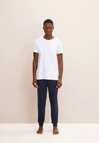 Vit T-shirt med korta ärmar och bröstficka, kombinerad med marinblå joggerbyxor. Båda plaggen är gjorda av mjukt, lätt tyg.