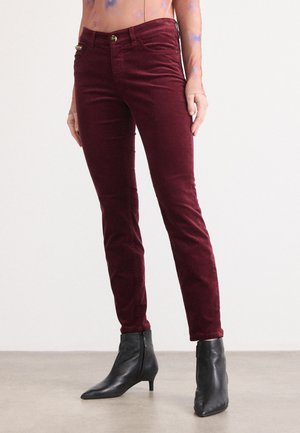Bordeauxkleurige corduroy slim-fit broek met een knoopsluiting, voorzakken en minimale stikseldetails. Gecombineerd met zwarte enkellaarsjes.