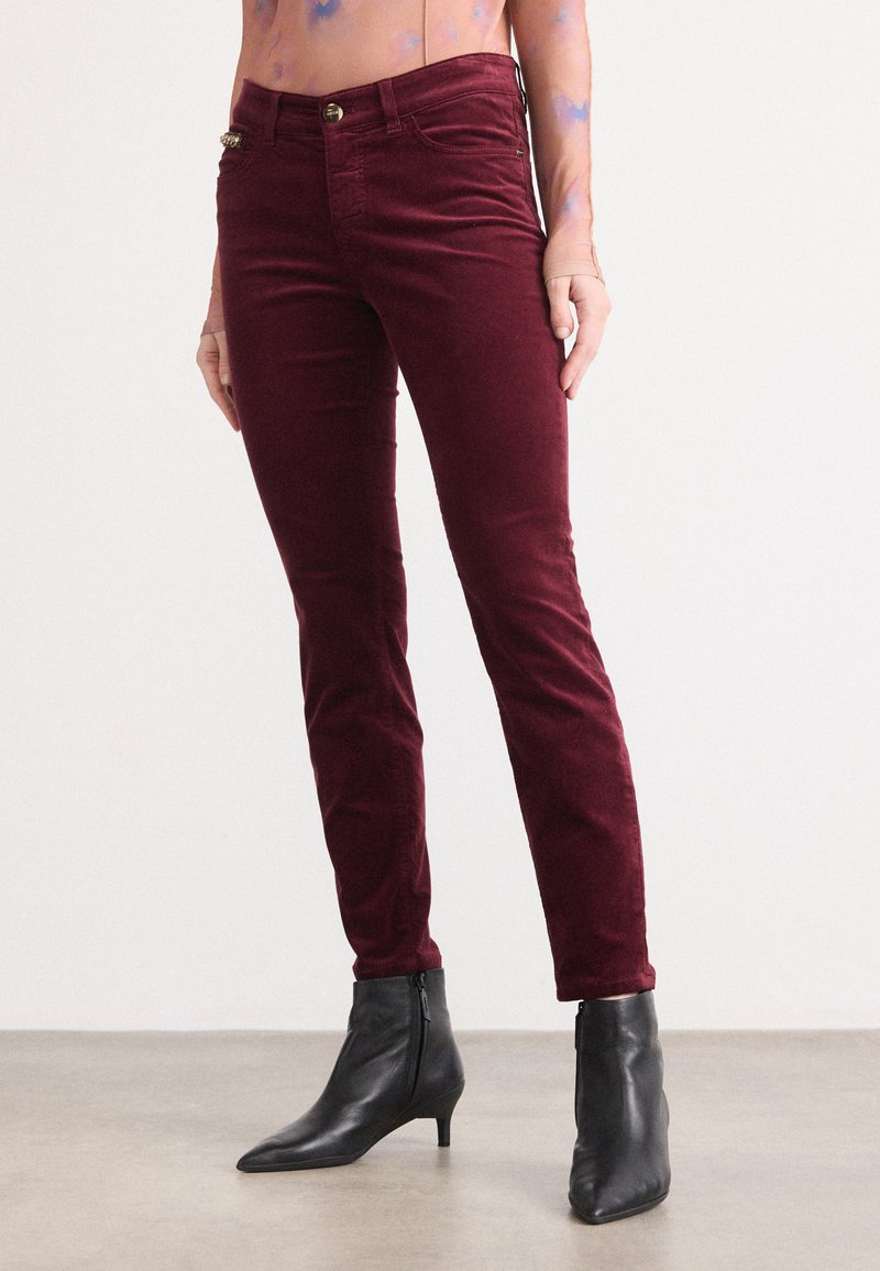 Bordové kordové slim-fit nohavice s gombíkovým zapínaním, prednými vreckami a minimálnymi stehmi. Skombinované s čiernymi členkovými topánkami.