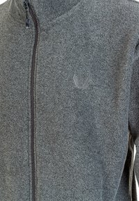 Giacca in pile grigia con colletto alto, chiusura a zip completa e ricamo del logo discreto. Il tessuto ha una finitura morbida e testurizzata.