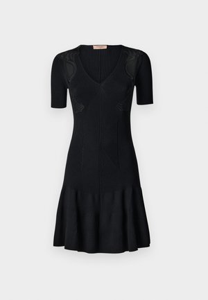 Musta ribattu neulemekko lyhyillä hihoilla, V-pääntiellä, levyämällä helmaa ja teksturoitua yksityiskohtaa vartalolla. Suora, vartalonmyötäinen muotoilu.