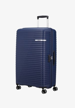 Valigia rigida blu navy con texture a righe orizzontali, ruote duali, manico estraibile e sistema di chiusura integrato sul lato.