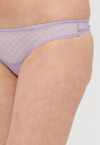 Tanga de malla lila claro con un patrón de puntos, con un borde festoneado y una cinturilla plana. Tela suave y texturizada.