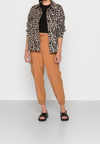 Chaqueta de leopardo hecha de material suave, top negro ajustado, pantalones cargo color arena con puños elásticos y sandalias negras.