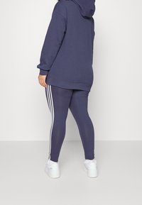 Námořnická modrá oversized mikina s kapucí, v kombinaci s námořnickými legínami s bílými bočními pruhy a bílými sportovními botami.