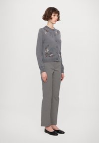 Szürke kardigán virágmintás hímzéssel és gombdíszekkel, fekete-fehér mintás nadrággal és fekete lapos cipővel kombinálva.