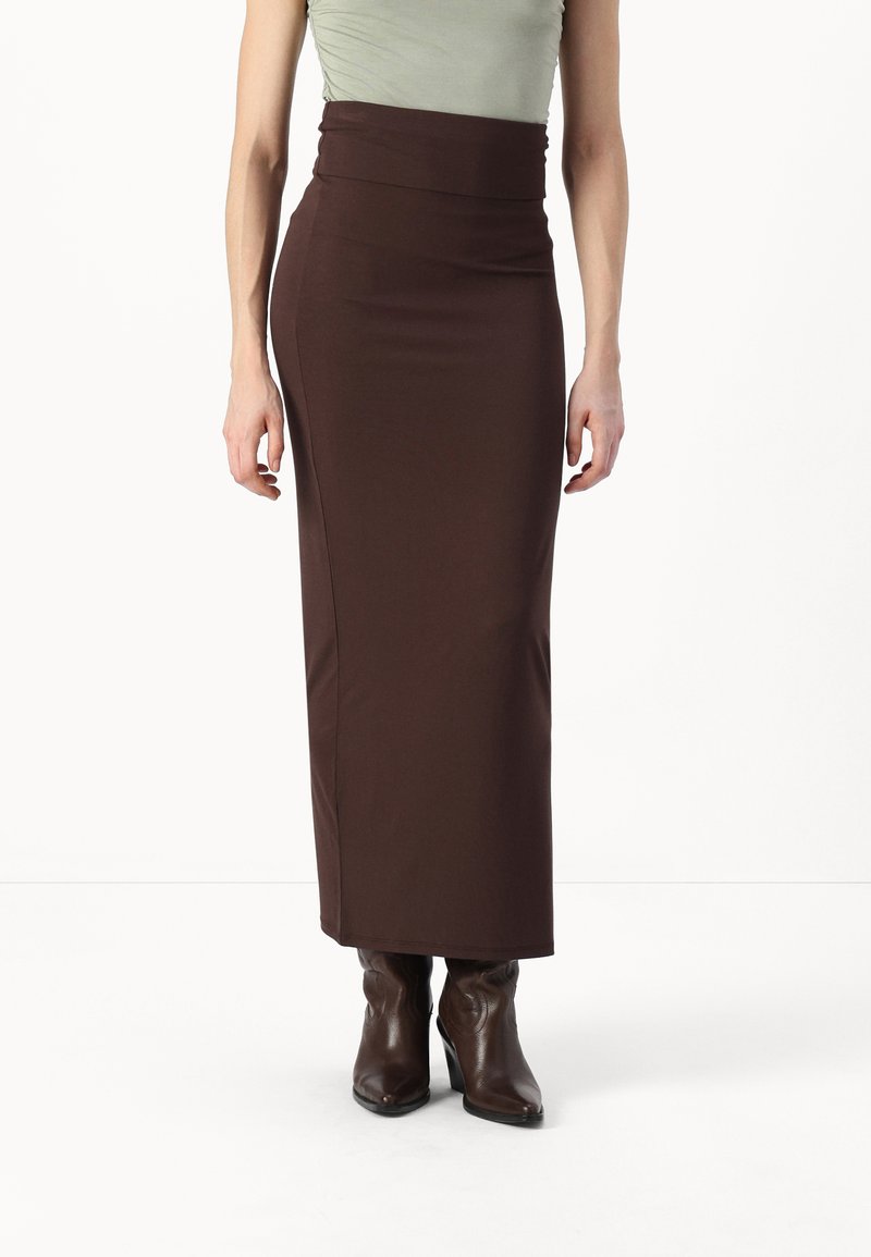 Fustă maro, ajustată, de lungime până la genunchi, cu talie înaltă și textură netedă, asociată cu cizme negre cu toc pentru un aspect elegant.