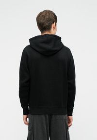 Čierna mikina s uvoľneným strihom, s veľkou kapucňou a rebrovanými manžetami. Hladký povrch, minimalistický dizajn, jednoduchý zadný pohľad.