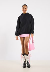Felpa nera oversize, gonna mini rosa, stivali da cowboy bianchi e neri con dettagli rosa, borsa rosa. Outfit urbano semplice e casual.