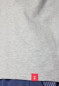 Γκρι κοντομάνικο μπλουζάκι από μαλακό βαμβάκι, με μια μικρή κόκκινη ετικέτα με σχέδιο ζικ-ζακ στο κάτω στρίφωμα.