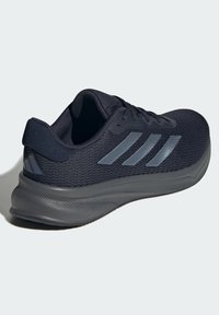 Zapatilla deportiva azul marino con parte superior de malla, suela texturizada negra y tres rayas grises en el costado para la marca.