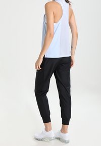 Lichtblauw mouwloos tanktop met mesh achterkant; zwarte joggerbroeken met ribbels aan de enkels; witte sneakers; sportieve activewear-design.