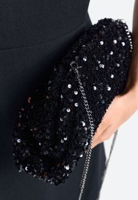 Fekete flitterekkel díszített, kerek formájú clutch táska, láncos pánttal és fém csattal. Texturált felület, fénylő flitterekkel.