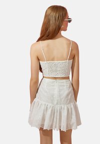 Conjunto blanco de dos piezas que incluye un top recortado y fruncido con tirantes finos y una falda acampanada con bordados florales y un dobladillo con volantes.