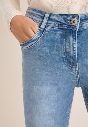 Hellblaue Jeans aus Denim mit einem verwaschenen Finish, ausgestattet mit einer Fronttasche und einem Knopfverschluss an der Taille. Die Nähte sind entlang der Kanten sichtbar.