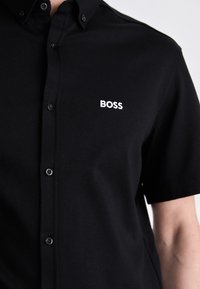 Polo shirt nero in misto cotone, con colletto a punta, chiusura a bottoni e logo ricamato bianco sul petto. Morbido al tatto.