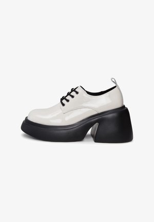 Witte lakleren veterschoenen met een stevige zwarte platformhak. Voorzien van zwarte veters en een lusvormige haklus. Glad van textuur.