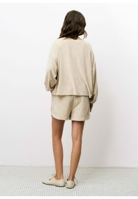 Beige katoenen pullover met verlaagde schouders en een cropped lengte, gecombineerd met bijpassende beige shorts. Eenvoudig ontwerp, zachte textuur.