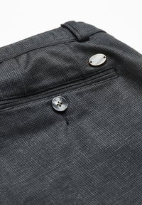 Tissu à carreaux gris avec une poche arrière, un bouton noir marqué "bugatti" et une plaque ovale en métal "bugatti" au-dessus de la poche.