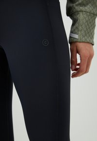 Visoko zmogljive črne leggins hlače, izdelane iz raztegljivega materiala, z majhnim logotipom ob strani in gladko mat površino.