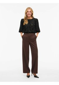 Svart teksturert bluse med 3/4-lange ermer, kombinert med høyhuskede brune vide bukser og svarte spisse hæler.