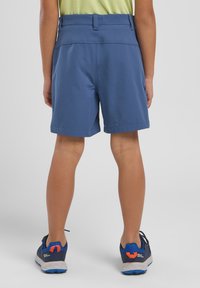 Pantalones cortos azules hechos de una tela ligera con cintura y parte delantera plana. Llevados con zapatillas deportivas grises y azules con acentos naranjas.