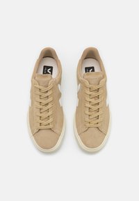 Tan suede sneakers with white accents, featuring a lace-up design, round toe, and cushioned insole. Smooth texture, minimalist style.