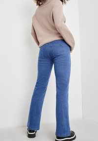 Suéter tejido, acanalado, de color rosa claro con un cuello alto, combinado con vaqueros acampanados azules. Los vaqueros cuentan con cinco bolsillos y costuras visibles.