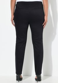 Schwarze maßgeschneiderte Hose mit glatter Textur, geradem Bein Design und zwei Gesäßtaschen, kombiniert mit high heels.