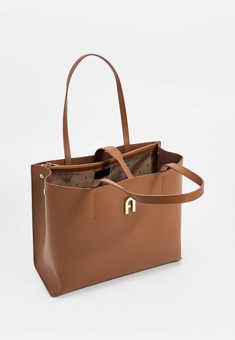 Brązowa skórzana torba tote z podwójnymi uchwytami, złotym logo akcentującym, otwartym wierzchem i podszewką z tkaniny z delikatnym wzorem.