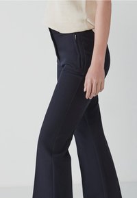 Marineblauwe flared broek met een getailleerde pasvorm, voorzien van zijzakken met strakke ritsen, gemaakt van een gladde, textuurstoffen.